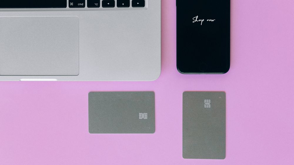 Laptop, cards, and smartphone on pink background for online shopping.