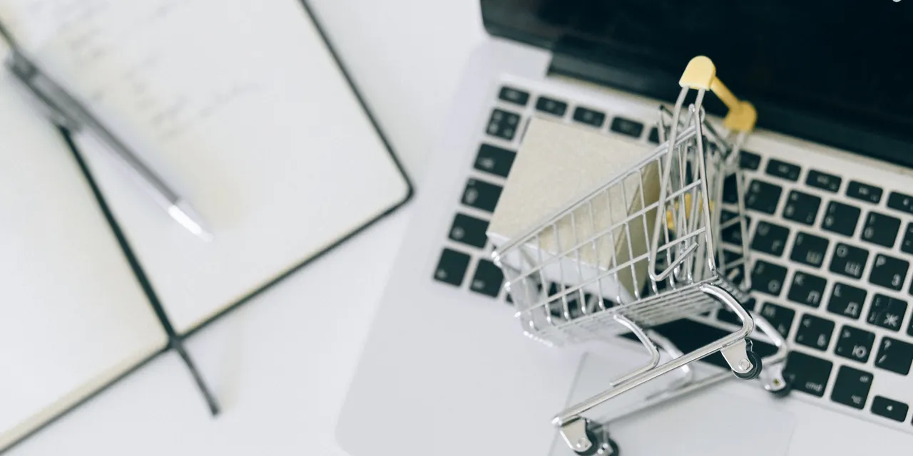 A miniature shopping cart resting on a laptop keyboard, representing GEO in product searching and AI shopping recommendations
