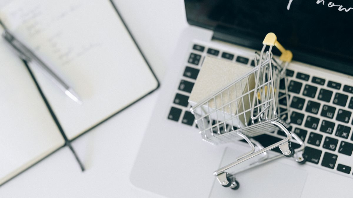 Carrinho de compras em miniatura sobre o teclado de um notebook, representando compras online