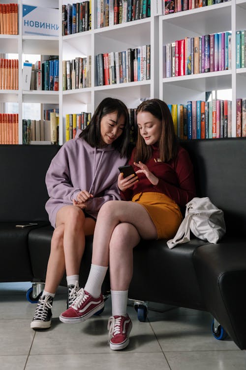 Free Two Teenagers Sitting on a Couch Looking at a Smartphone Stock Photo