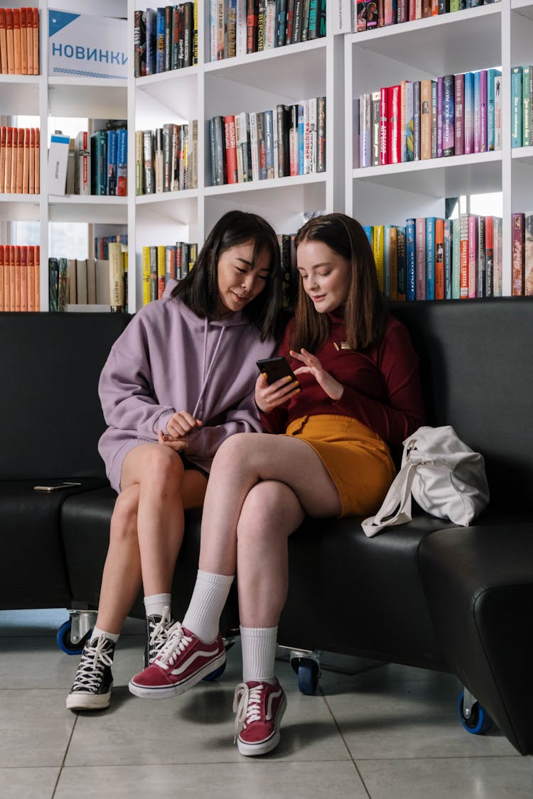 Two Teenagers Sitting On A Couch Looking At A Smartphone