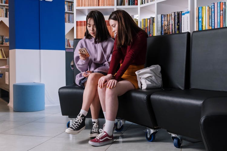 Two Teenagers Sitting On A Couch Looking At A Smartphone