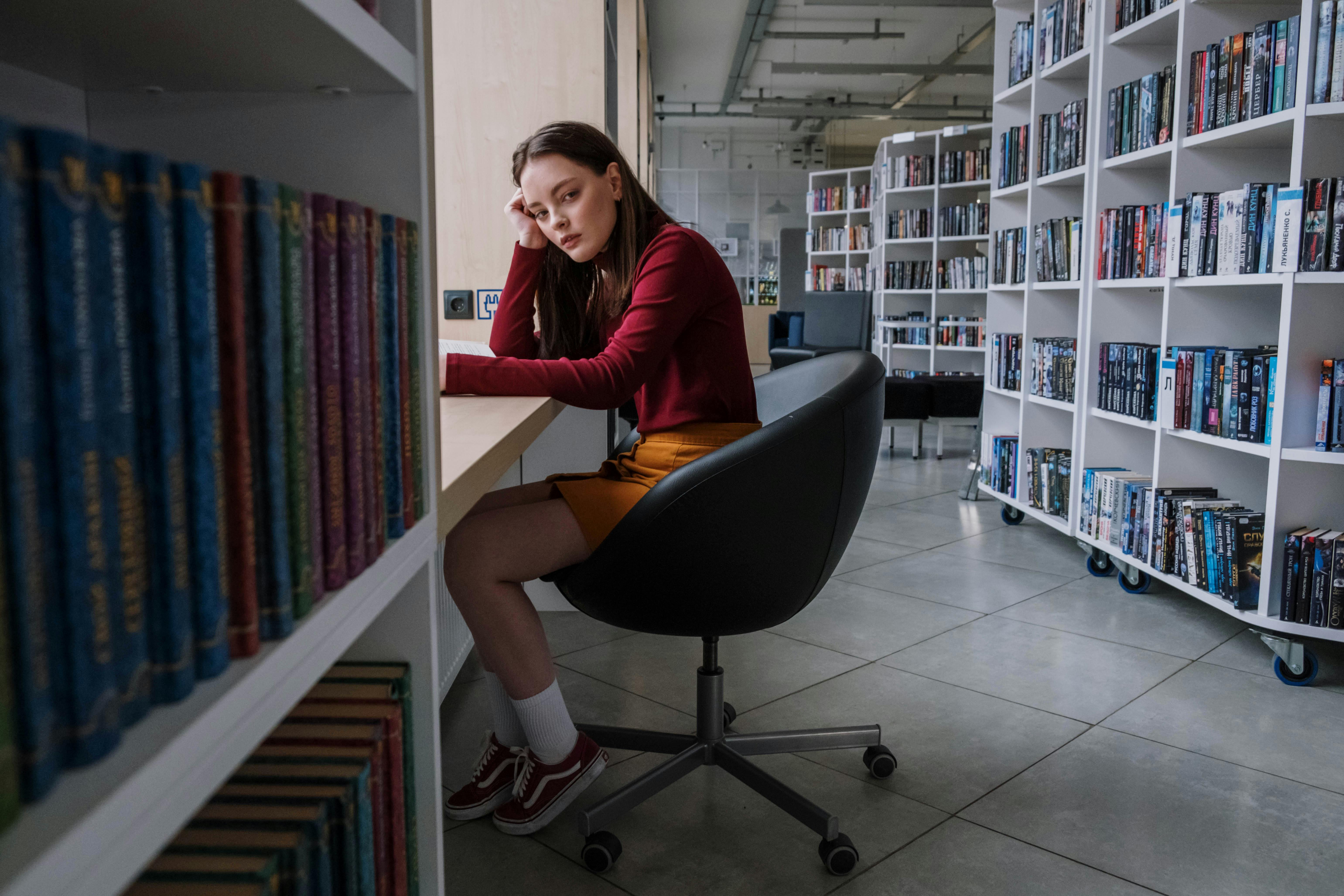 a female teenager sitting on a black chair inside the library