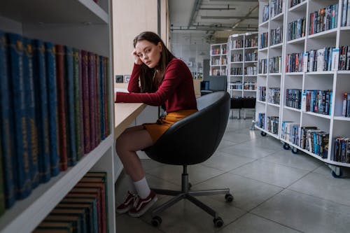 A Female Teenager Sitting on a Black Chair Inside the Library