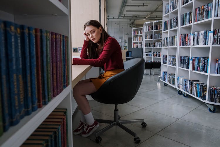 A Female Teenager Sitting On A Black Chair Inside The Library