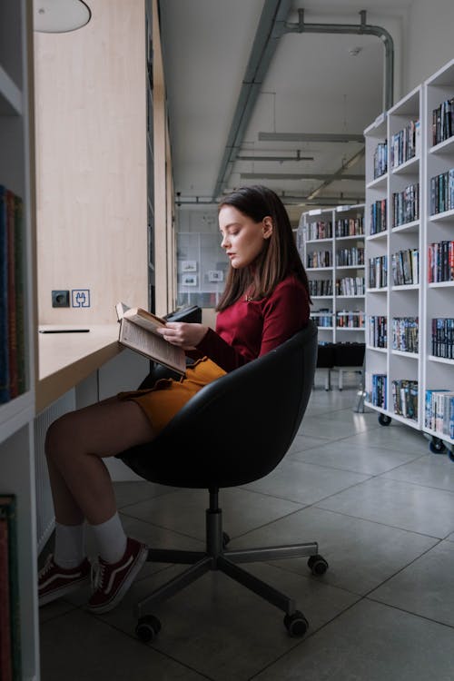 Free A teenage girl immersed in reading a book while sitting in a modern library. Stock Photo