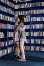 Woman in Gray Coat Standing Beside Bookshelf
