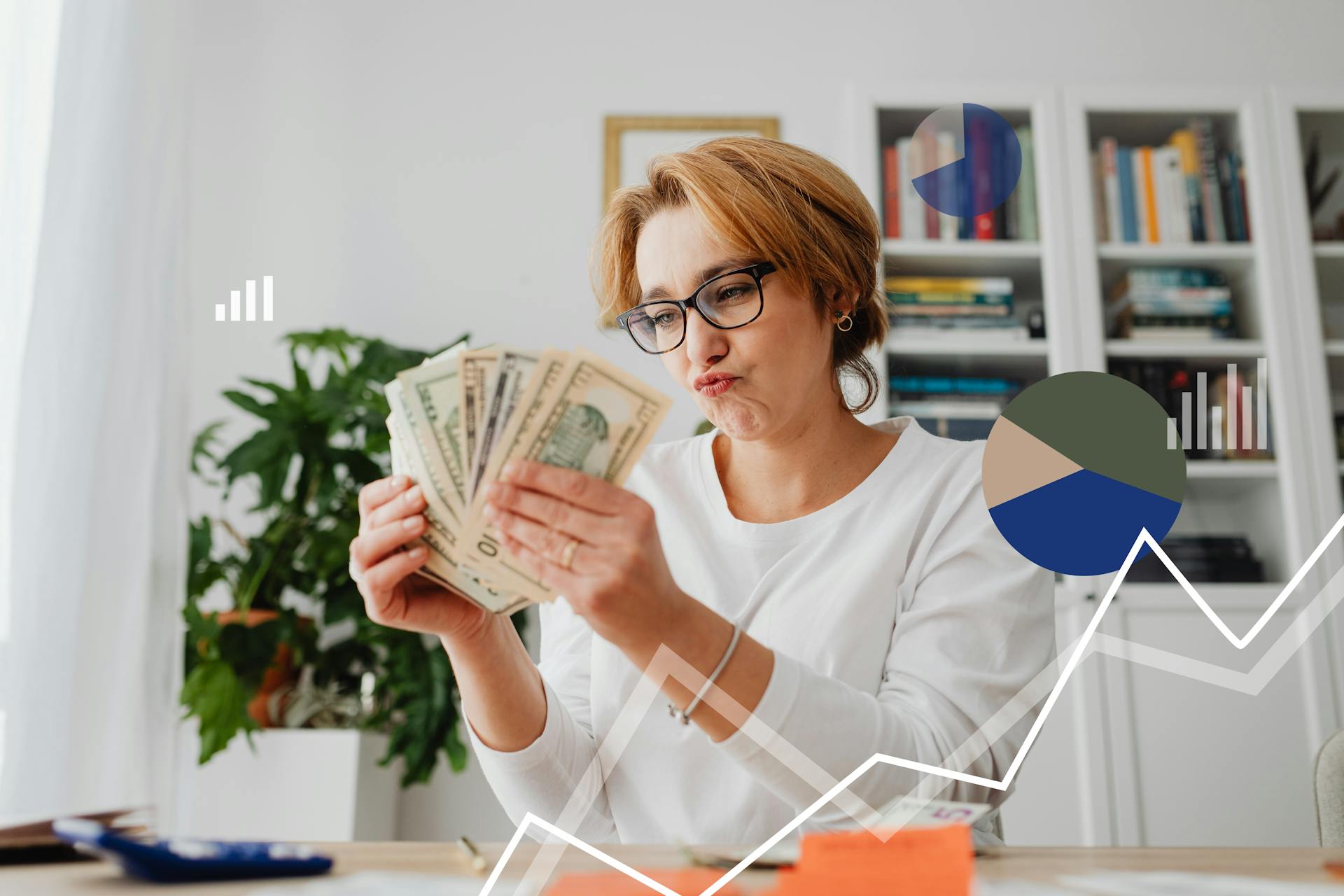 Woman in glasses counting money indoors with financial charts in the background.