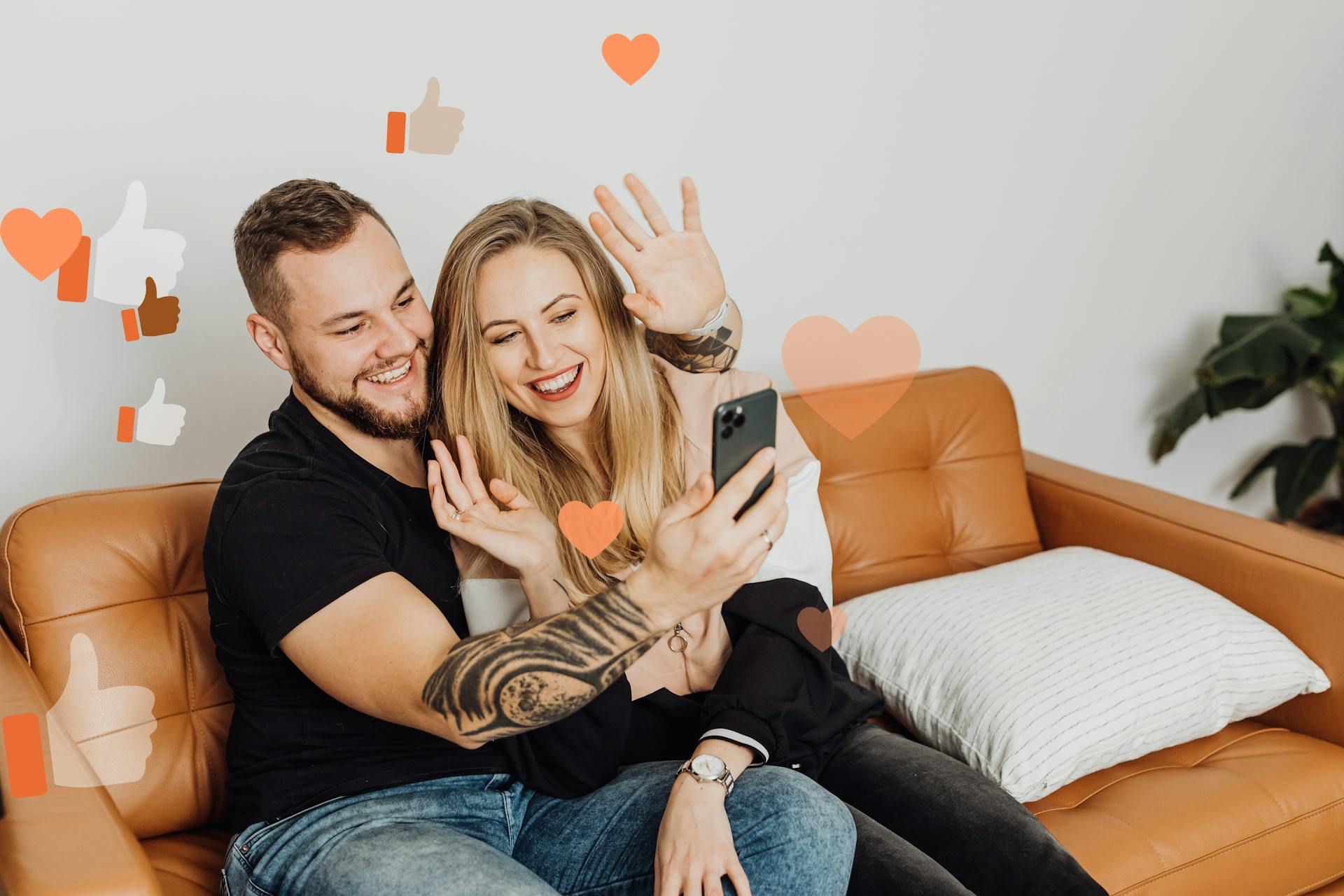 A smiling couple takes a selfie video call at home with digital social media icons overlay.