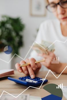 Woman using calculator with financial graph overlay, indicating data analysis and finance planning.
