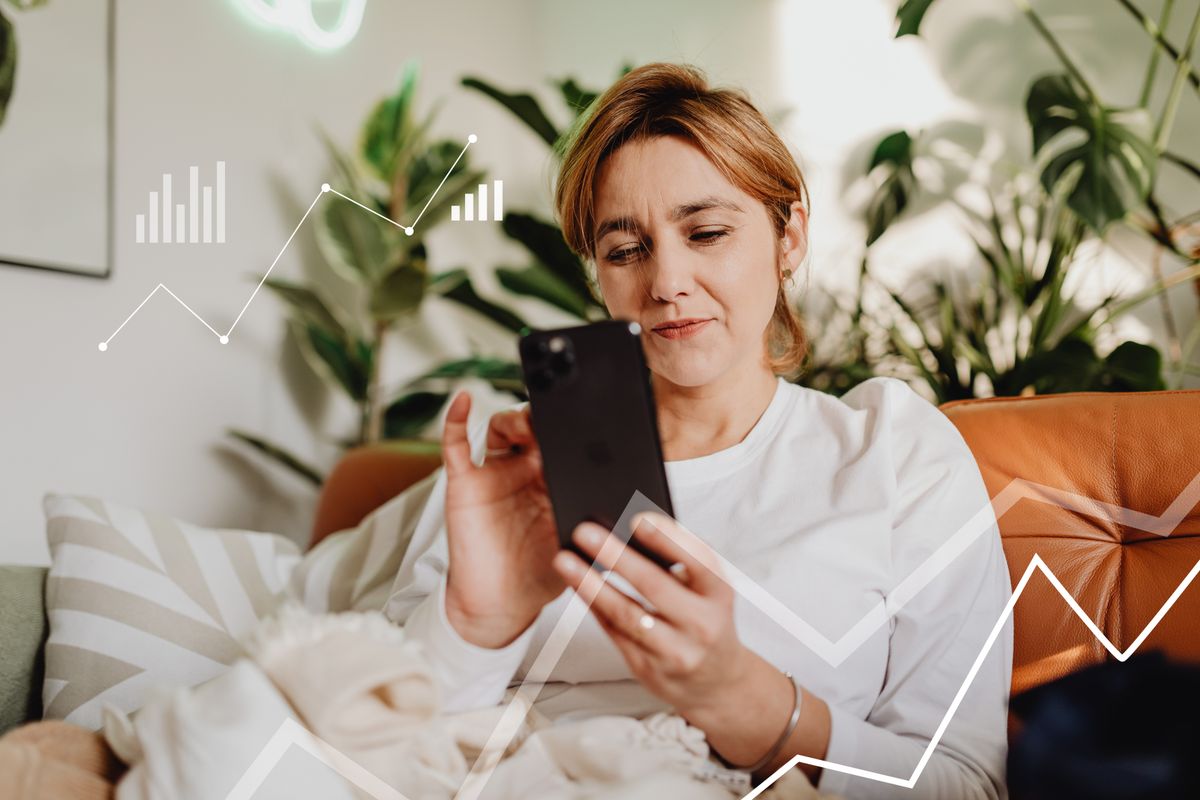 Akıllı telefon ekranında grafik gösteren kişi koltukta oturuyor