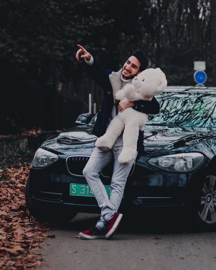 Man Standing Beside Black Car While Holding His Teddy Bear