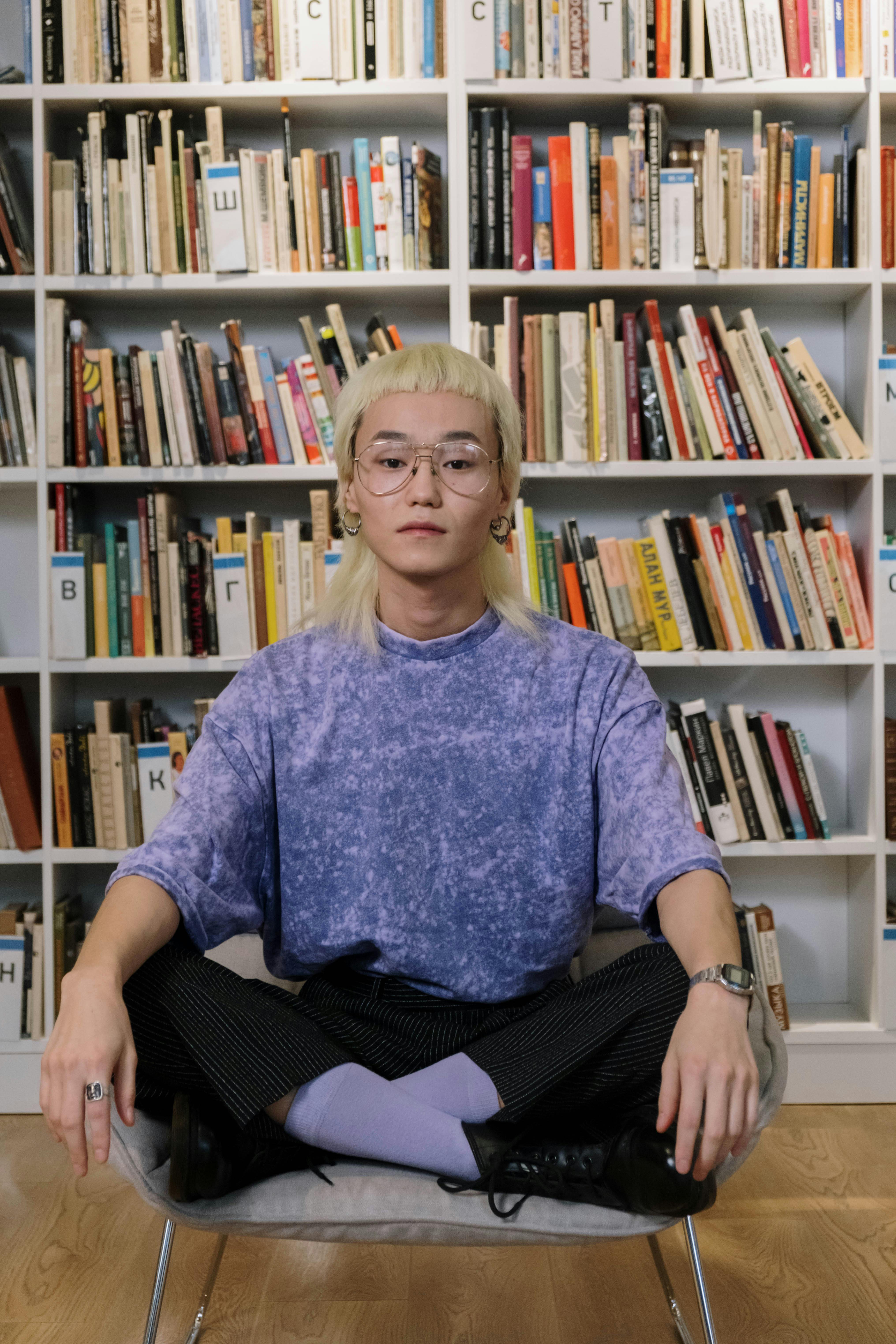 a young man in black pants sitting on the chair while wearing eyeglasses