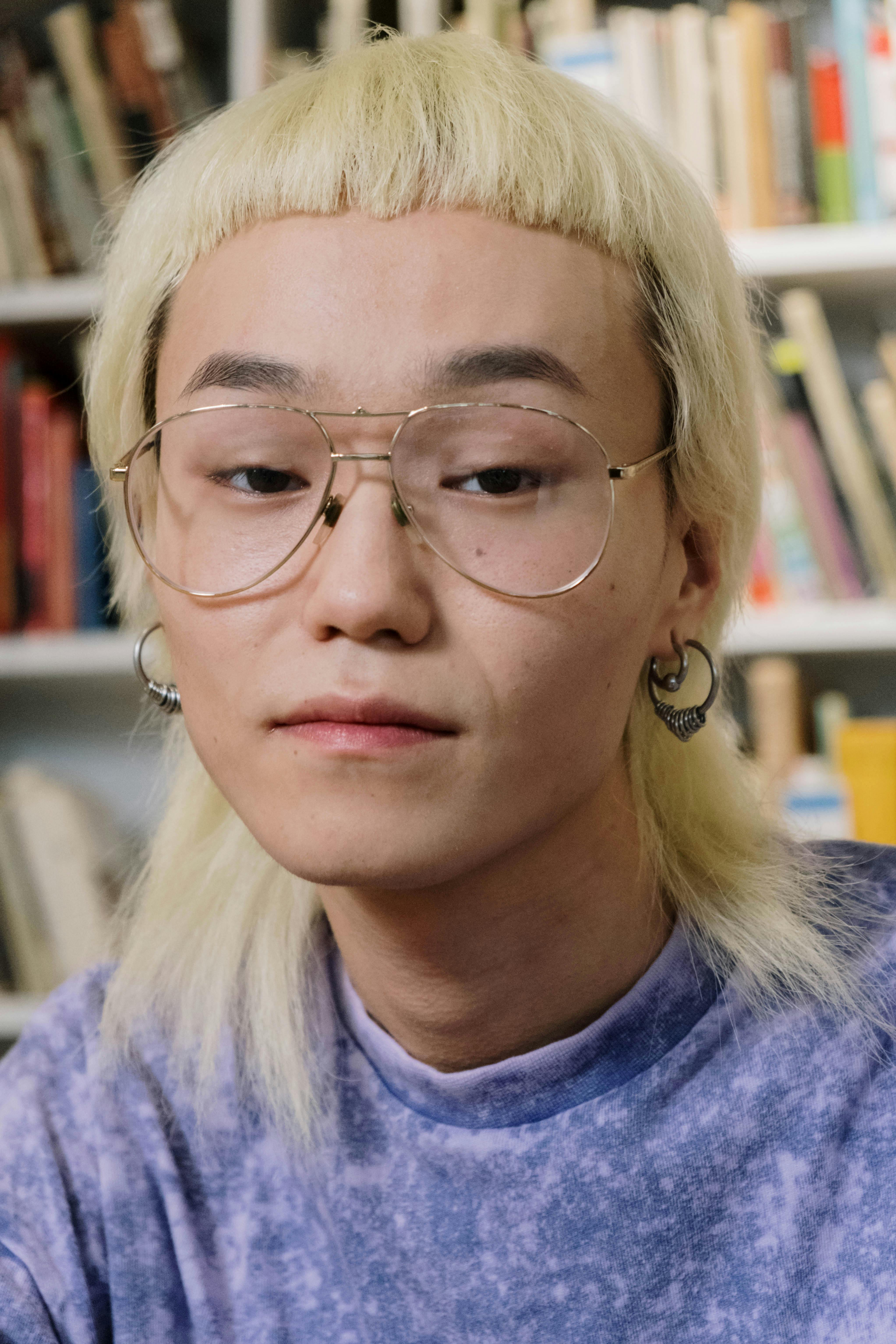Close-up portrait of a young person with glasses in front of bookshelves.