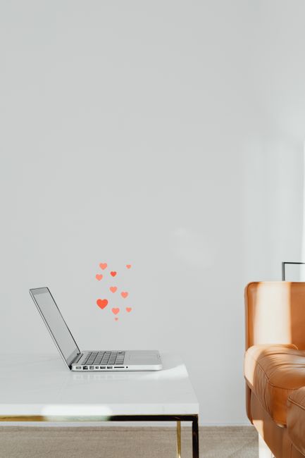 Sleek laptop on white table with heart stickers, minimalistic design.