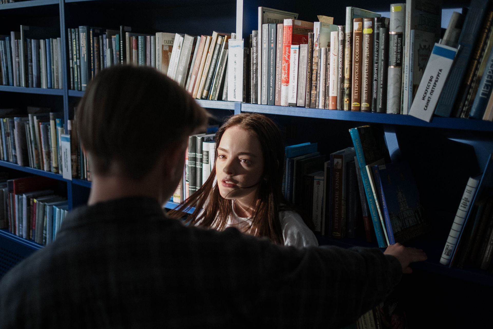 Teenagers having a conversation in a library with books on shelves.