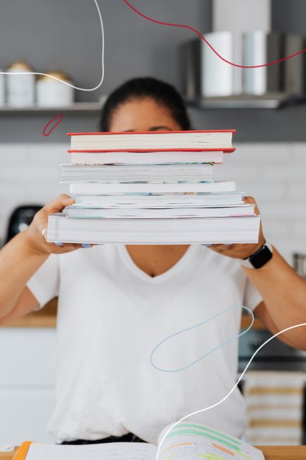 Adult holding a stack of books in a modern indoor environment, suggesting study or work.