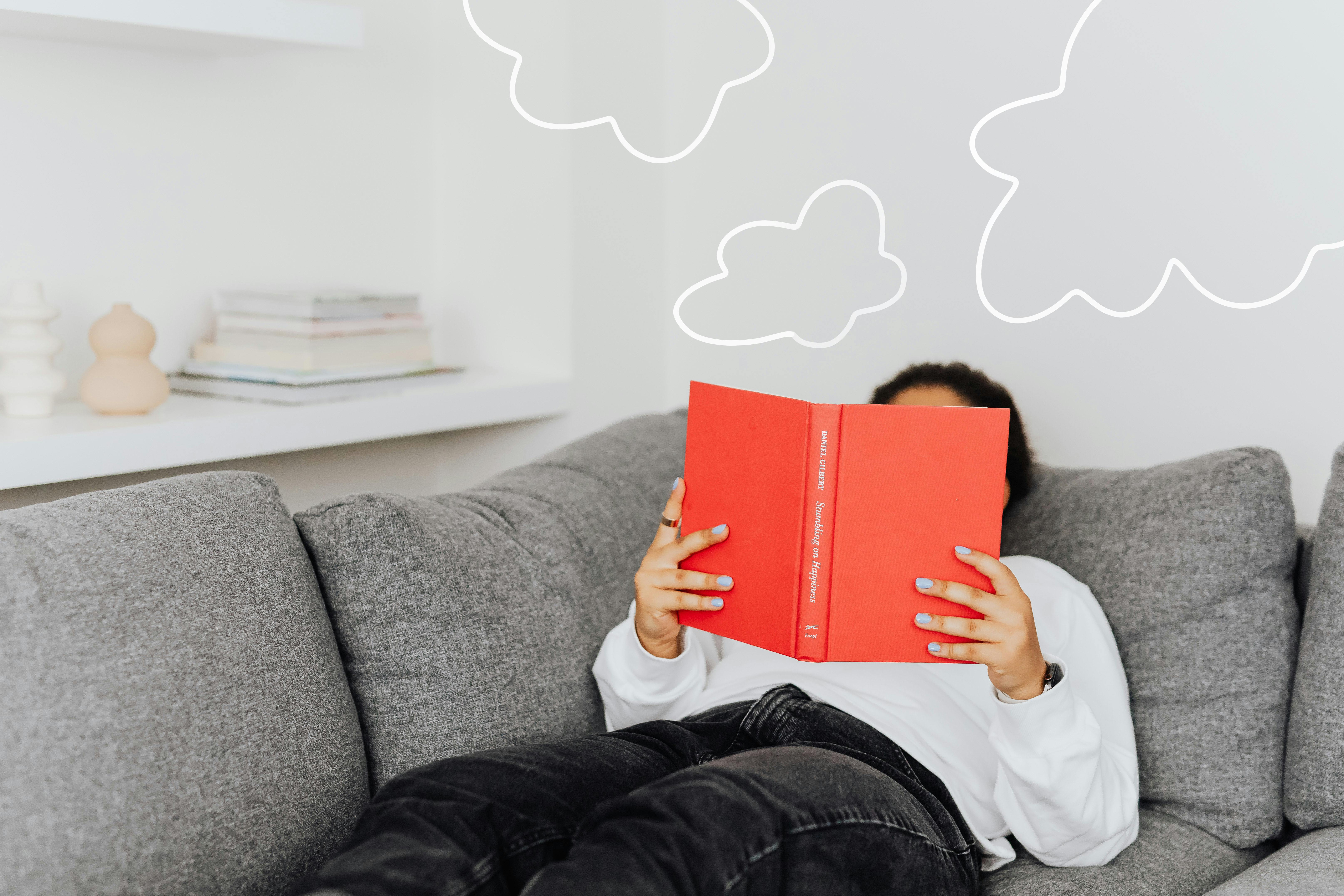 Person relaxing with a book on a sofa. Drawn clouds add a whimsical touch.