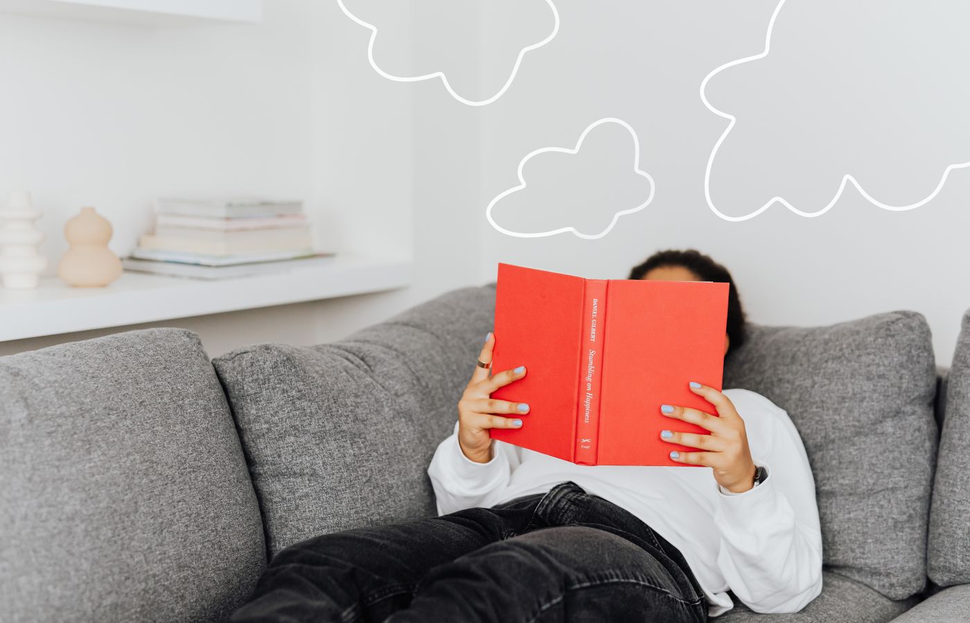 Person relaxing with a book on a sofa. Drawn clouds add a whimsical touch.