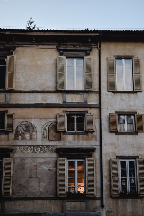 Free Detailed view of a historic building facade in Bergamo featuring ornate windows and shutters. Stock Photo