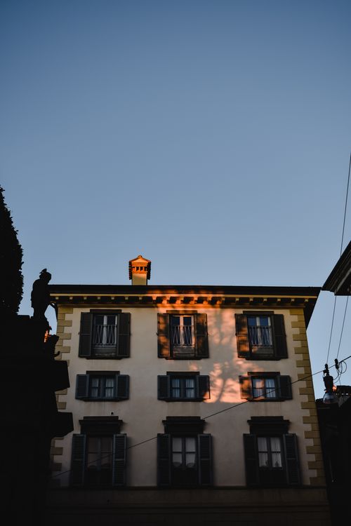 Free Elegant apartment building in Bergamo, Italy, adorned with warm sunset light and classic shutters. Stock Photo