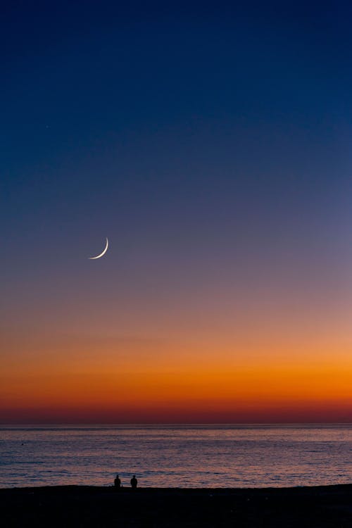 Crescent moon shining on bright sky with horizon line over rippling water near coast in tropical country at sundown time