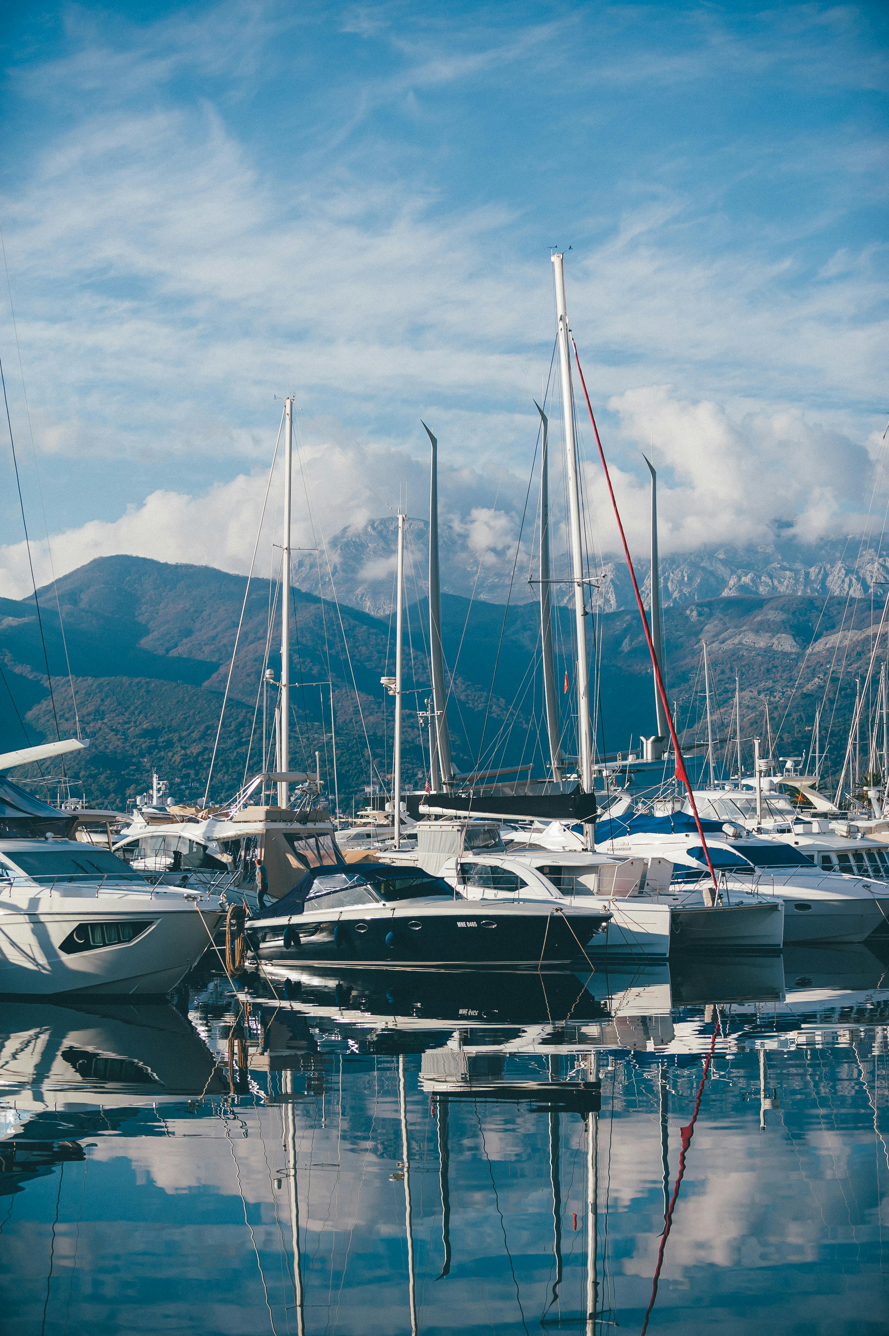 Free Scenic view of luxurious yachts docked in Tivat Marina with mountain reflections and clear blue skies. Stock Photo