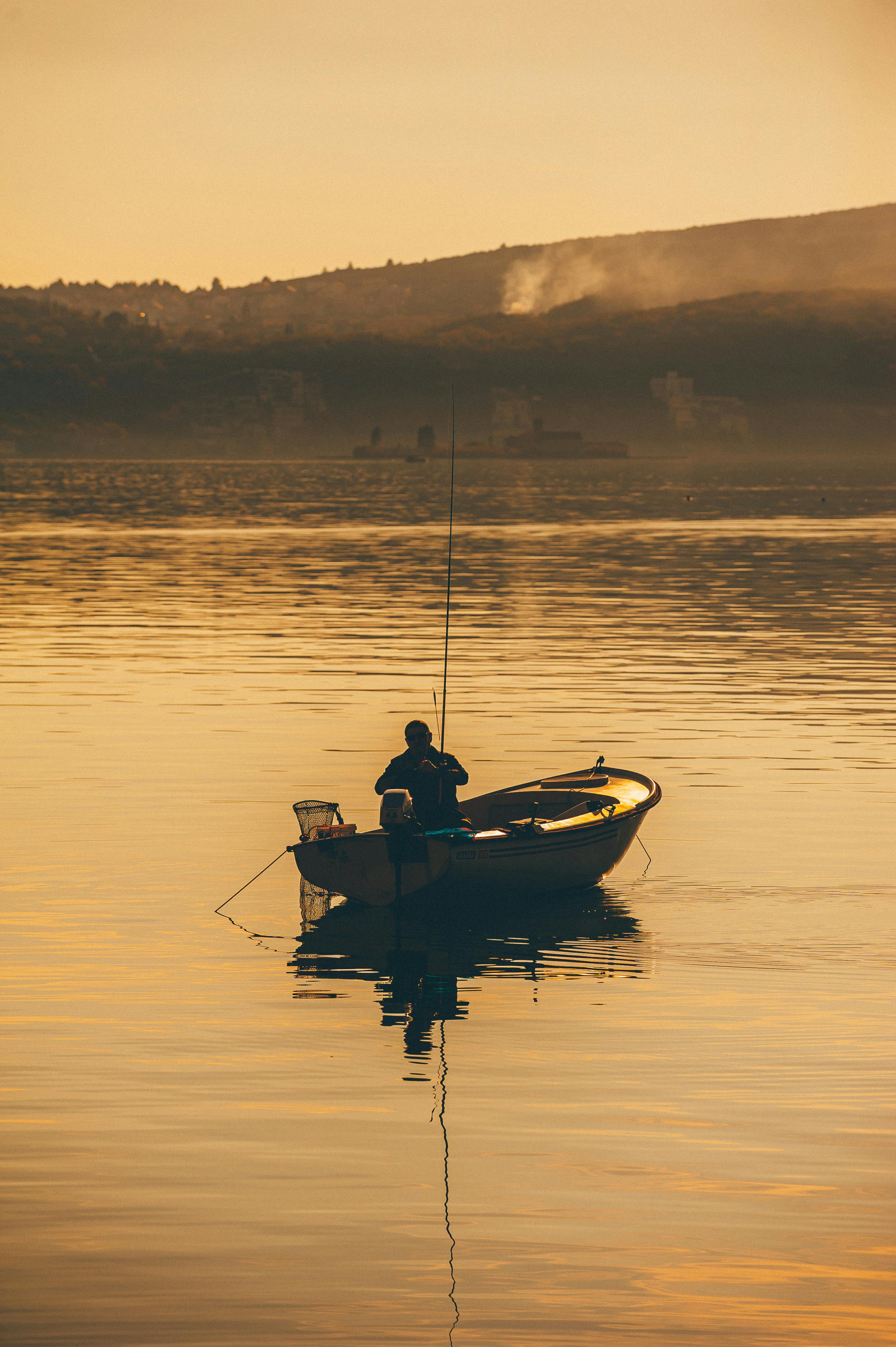 Free Angler fishing on a tranquil boat in Tivat, Montenegro during a golden sunset. Stock Photo
