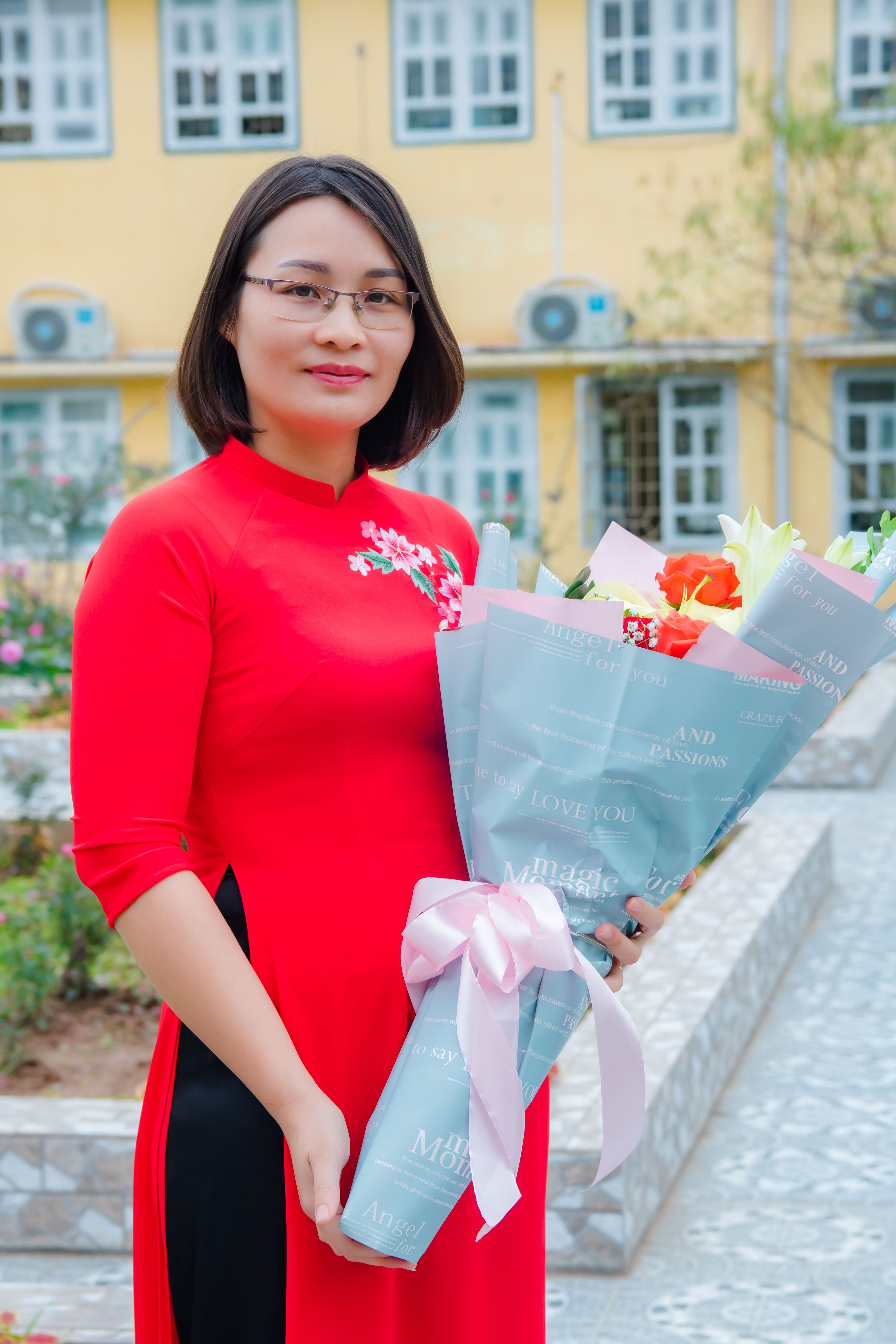 Elegant woman in red dress with eyeglasses holding a bouquet of flowers outside a building.