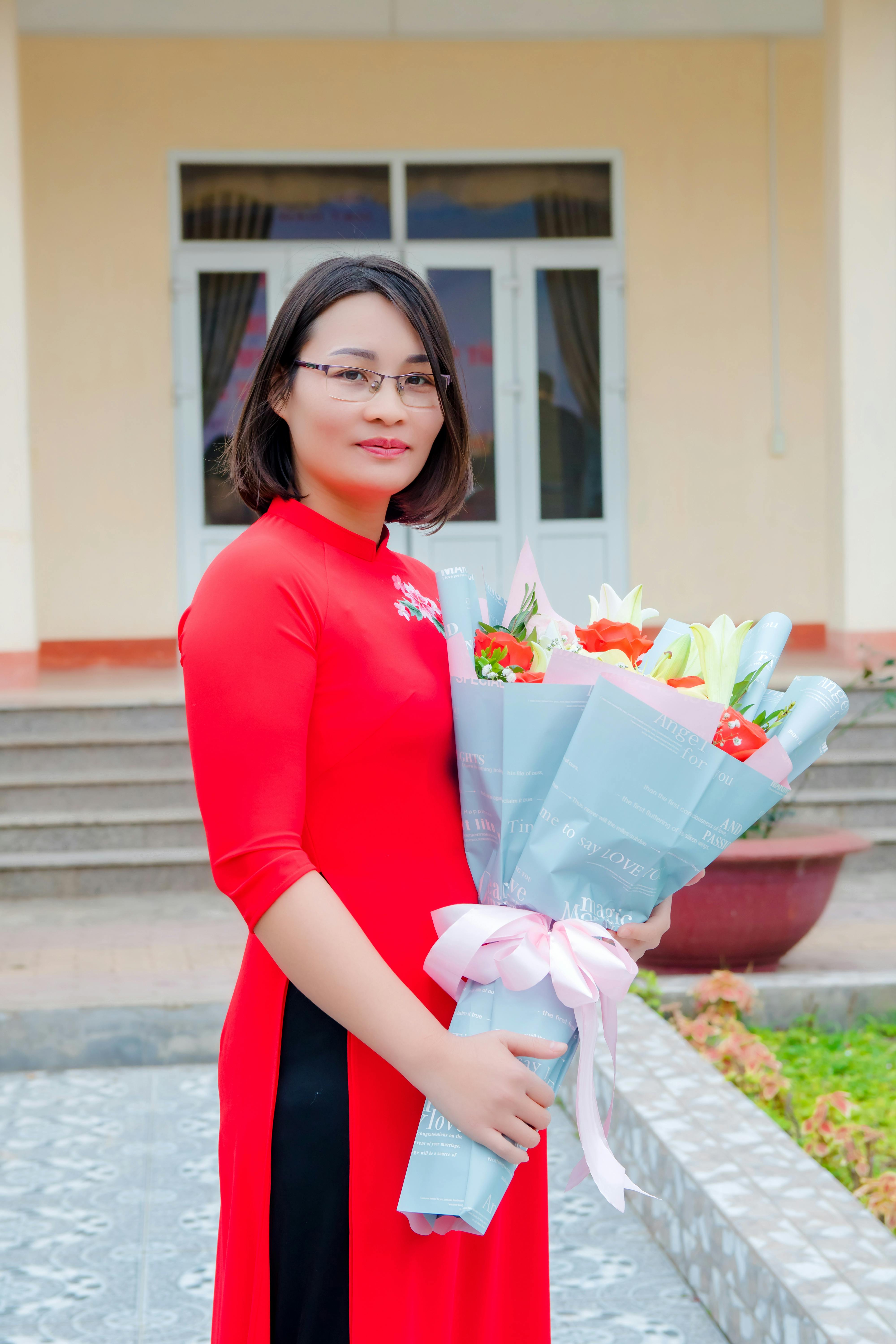 A woman in a red dress holding a colorful bouquet of flowers standing outside, conveying elegance and beauty.
