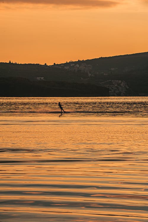 A Person Surfing on the Sea during Sunset