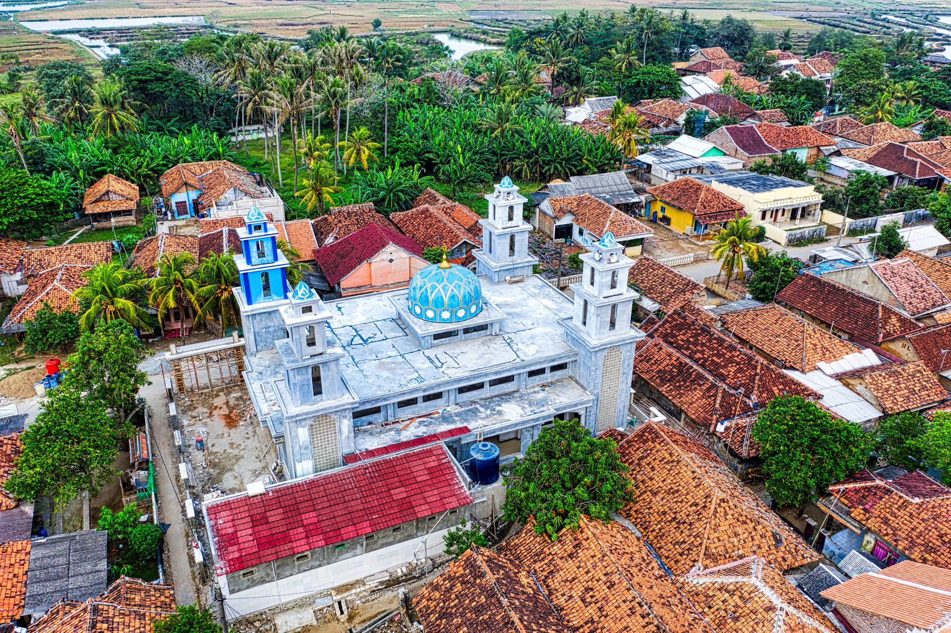 Drone view of aged residential houses with tilled clay rooftops located in town with mosque surrounded by tropical plants