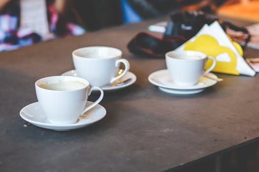 Three white coffee cups on a cafe table suggest a warm morning gathering.
