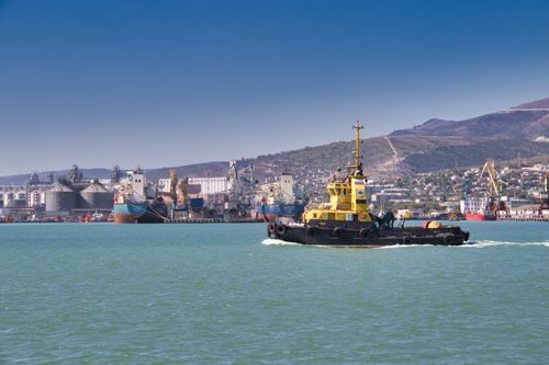 Free A dynamic view of a tugboat maneuvering through a busy industrial harbor on a sunny day. Stock Photo