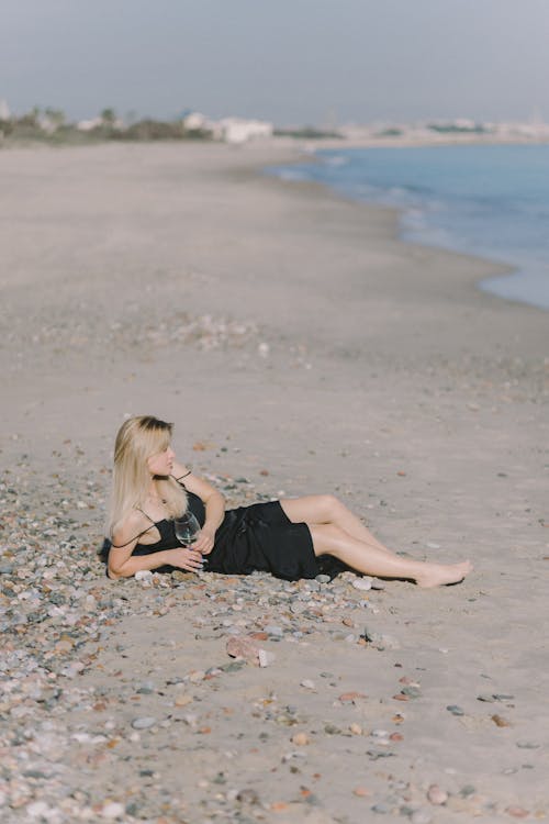 Woman Holding Wine Glass While Lying on Shore