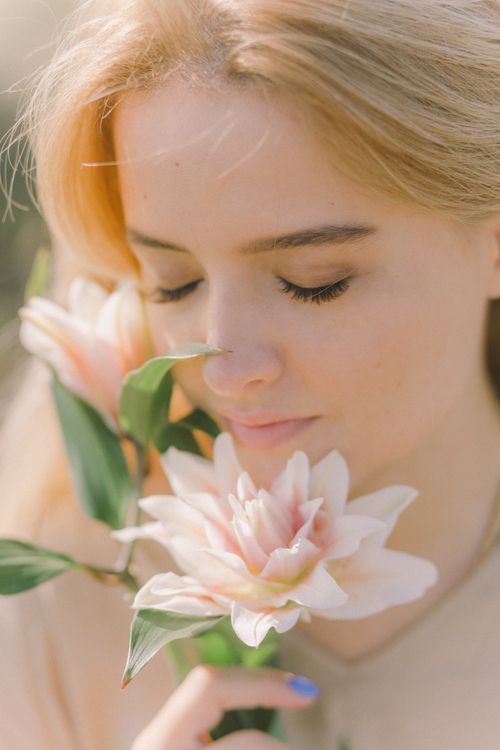 Free Close-up of a woman with closed eyes smelling blooming lilies outdoors on a sunny day. Stock Photo