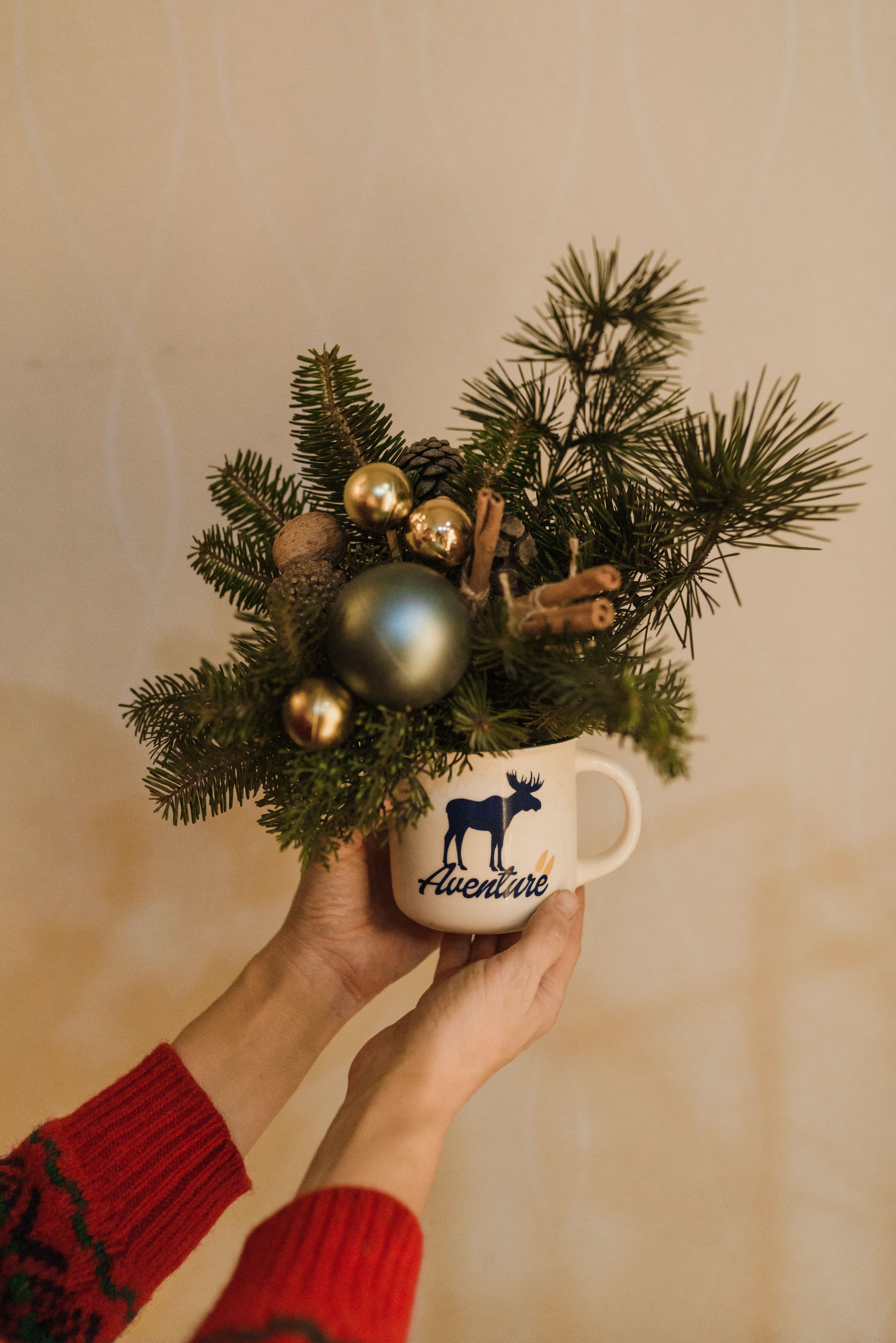 Hand holding a Christmas mug with greenery and ornaments, capturing holiday spirit.
