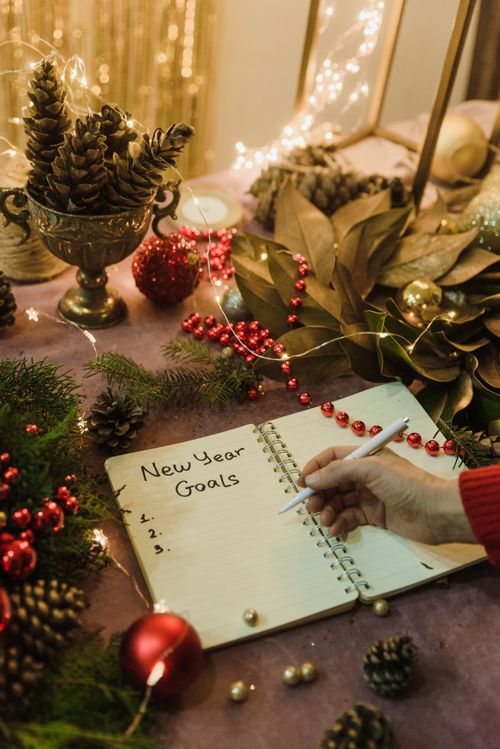 Free Hand writing New Year goals in a festive notebook surrounded by Christmas decorations and fairy lights indoors. Stock Photo