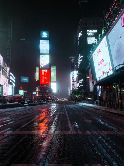 Free Moody night scene of an empty Times Square with illuminated billboards and wet streets reflecting lights. Stock Photo