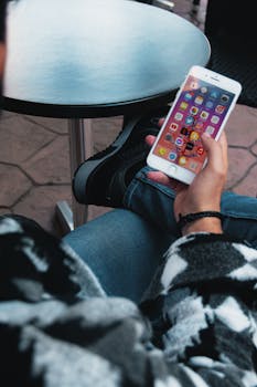 Close-up of a seated person using a smartphone at an outdoor cafe table.