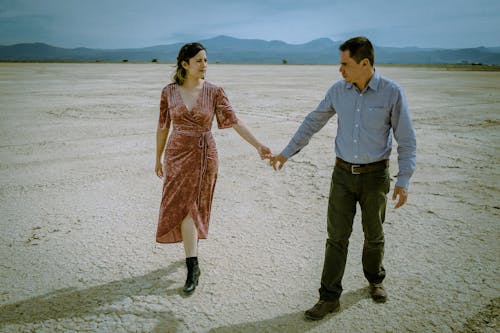 Man in Blue Button Up Long Sleeve Shirt Holding Hands With Woman in Pink Dress