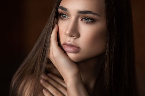 Free Crop young pondering female with natural makeup and sensitive lips touching cheek while looking away Stock Photo