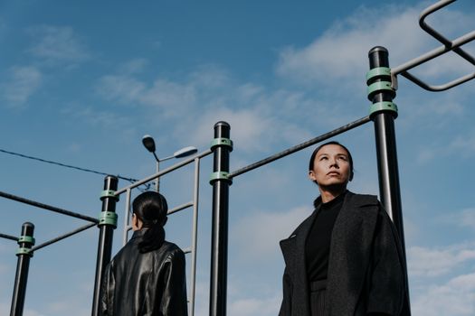 Two women posing fashionably at an urban gym under a clear blue sky.