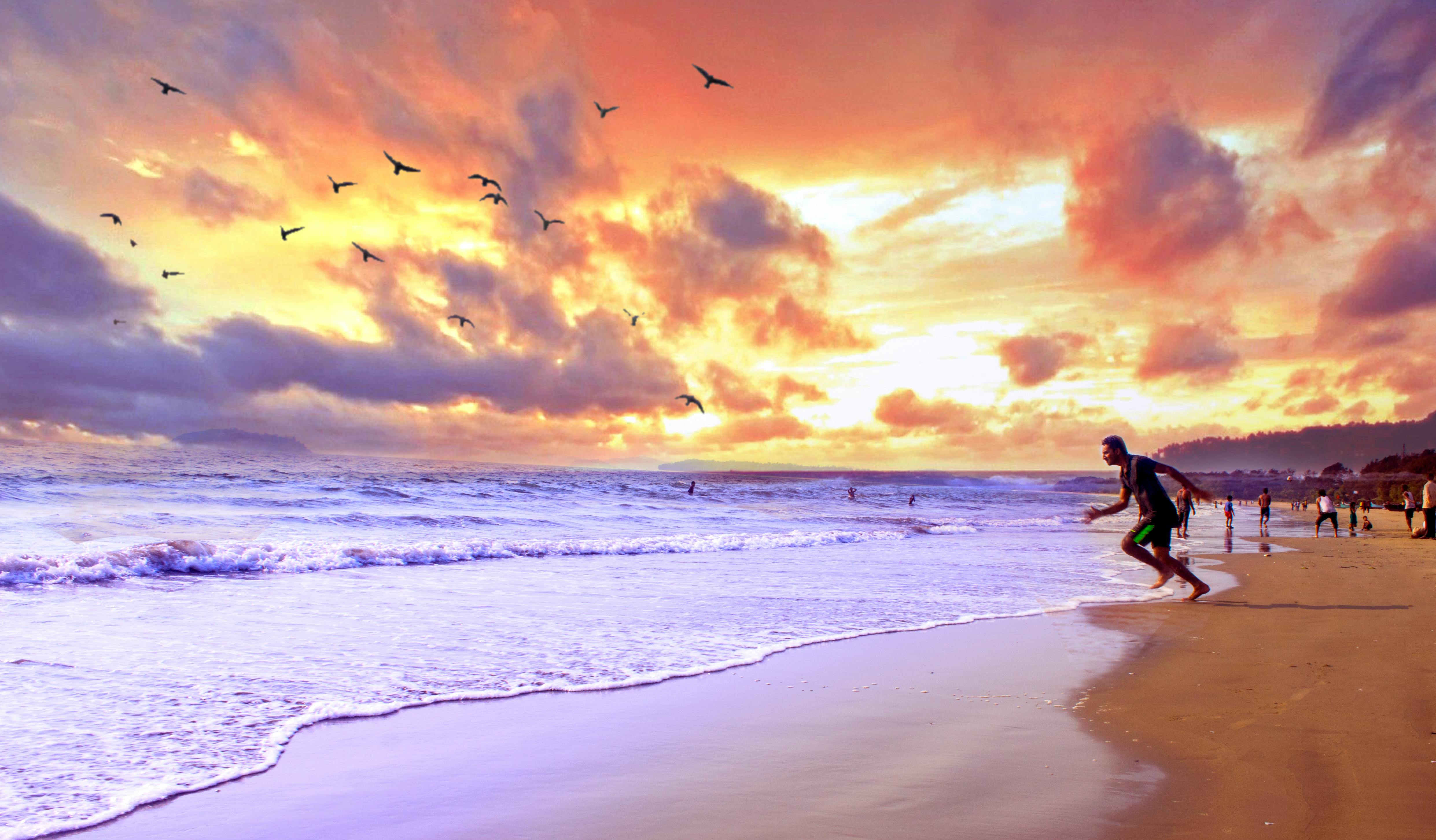 热闹的海滩上，美丽的日落中，人们享受着海浪，鸟儿在天空飞翔