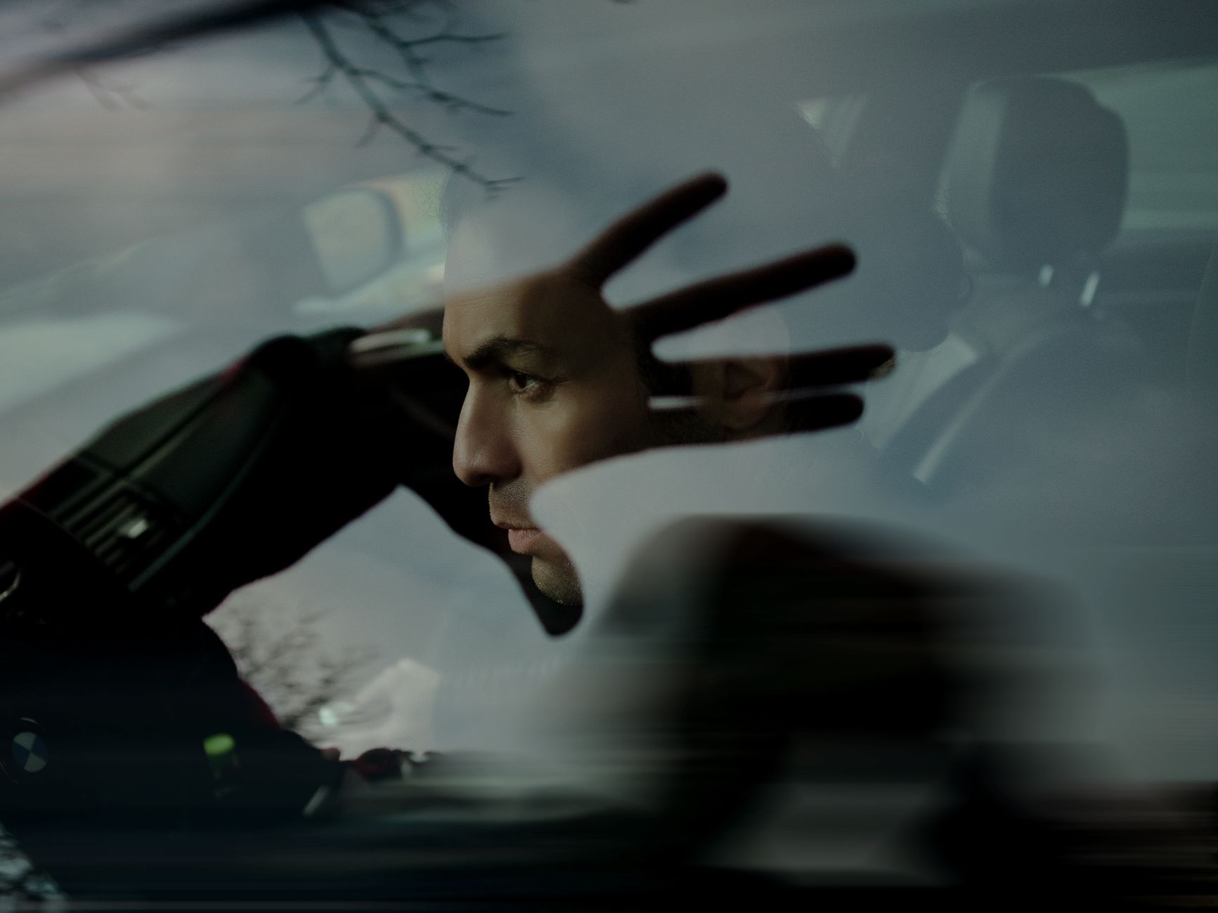 A man sits in a car with his silhouette dramatically reflected on the window.