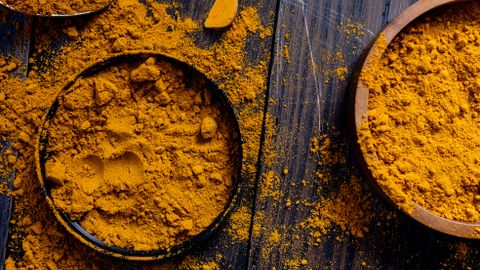 Close-up of turmeric powder in rustic bowls on a wooden surface, ideal for spice and food photography.