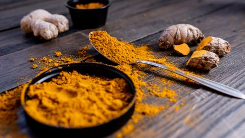 Vibrant turmeric powder and root arranged on a rustic wooden surface, showcasing culinary spice ingredients.