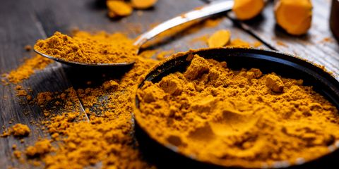 Close-up of vibrant turmeric powder with root on rustic wooden table, emphasizing texture and color.