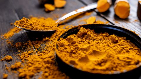 Close-up of vibrant turmeric powder with root on rustic wooden table, emphasizing texture and color.