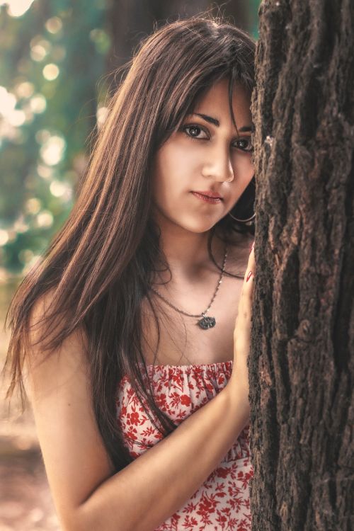 Free Woman leaning against a tree in a natural setting, expressing a serene mood. Stock Photo